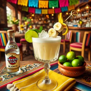 Een Mexicaans gepresenteerde cocktail genaamd 'Banana Daiquiri', geserveerd in een elegant cocktailglas met een romige lichtgele kleur. Het drankje is gemaakt van Havana Club Blanco, Crème de Bananes, limoensap, banaan en gemalen ijs. Het glas is gegarneerd met een decoratief prikkertje met een schijfje banaan, een schijfje limoen en een feestelijke stirrer. De tafel is versierd met kleurrijke Mexicaanse textiel, een kleine kleikom met limoenen en vrolijke decoraties. De achtergrond toont een levendige Mexicaanse setting met rustieke houten accenten, terracottategels en warm natuurlijk licht. Er is geen tekst of label zichtbaar op glazen, flessen of oppervlakken.