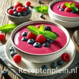 Lichte roze bosvruchtensoep met karnemelk, geserveerd in wit bord met verse bessen en muntblaadje.
